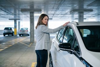 Femme évaluant une voiture électrique d'occasion compacte dans un parking urbain moderne