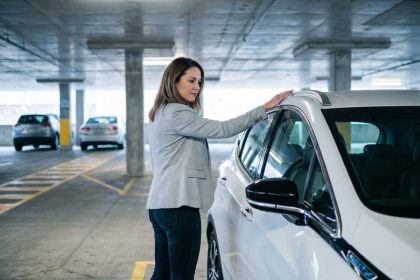 Femme évaluant une voiture électrique d'occasion compacte dans un parking urbain moderne